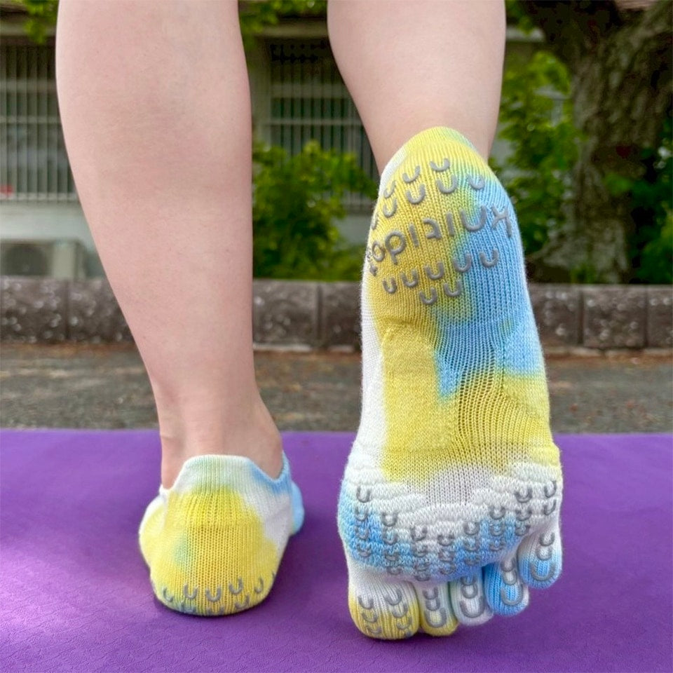 Feet wearing yellow and blue toe socks on a purple mat outdoors