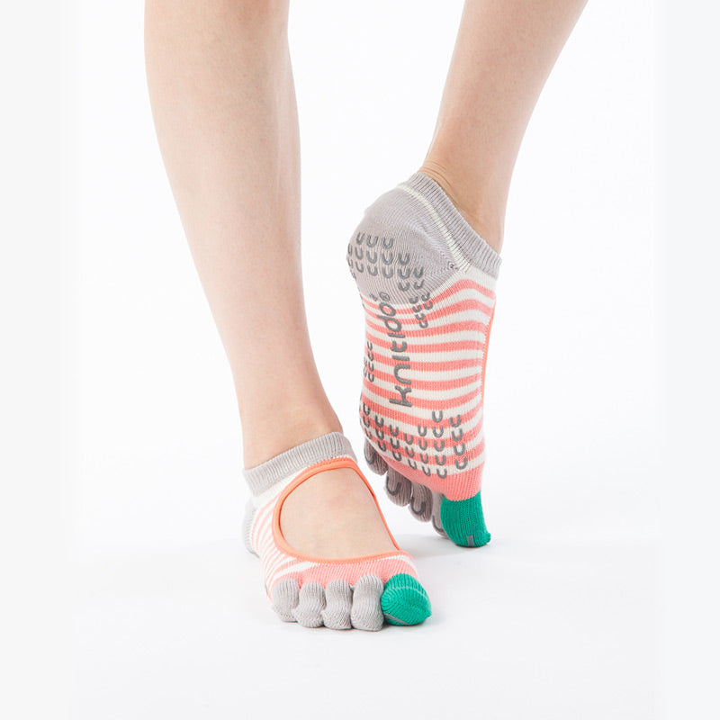 A pair of organic cotton toe liner socks with colorful stripes and grips on the sole, worn on human feet.