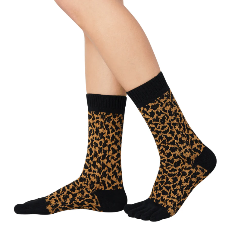 A pair of leopard print midcalf five toe socks worn on a person's feet, with the socks partially pulled down to show the toe separator design.