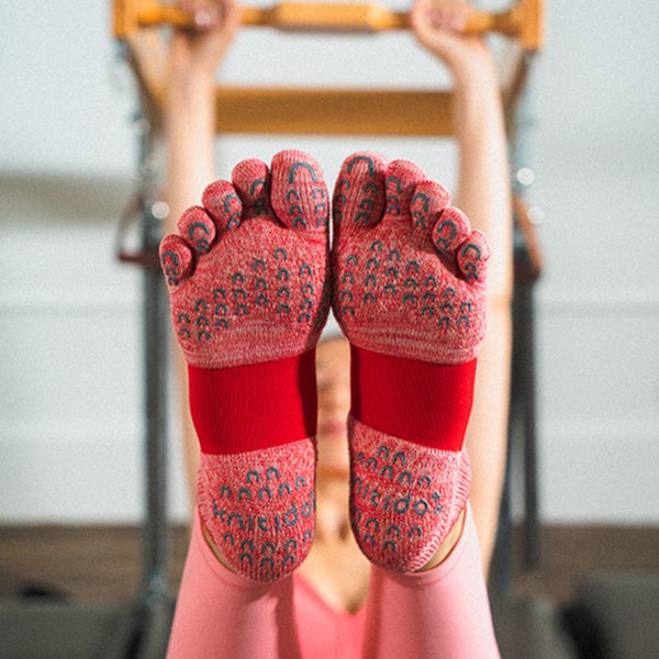 The sole of an instructor woman doing power yoga wearing Knitido plus brand Arch Support Heather Footie Grip Toe Socks With Power Pads product in red
