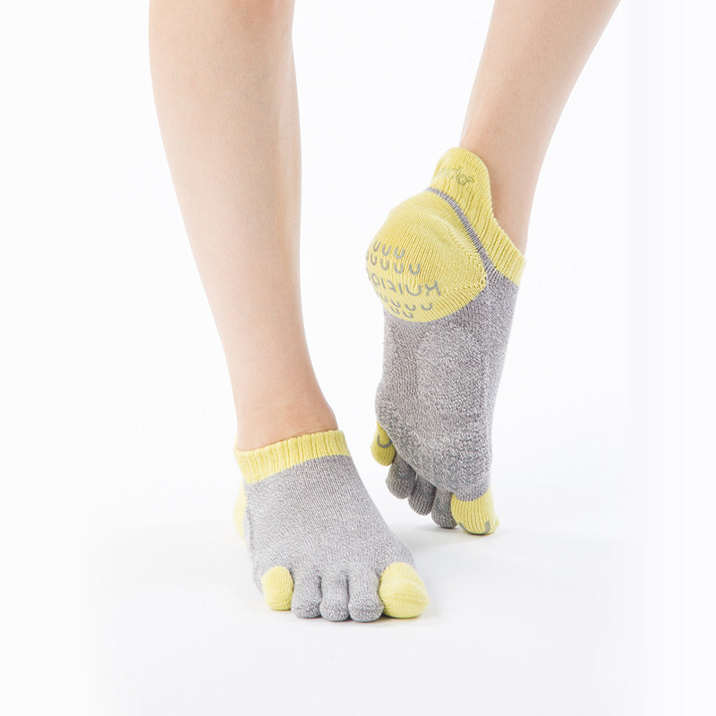 An oblique view of a leg wearing a pair of Knitido plus brand Two Colors Footie Grip Toe Socks With Power Pads in Grey and Yellow