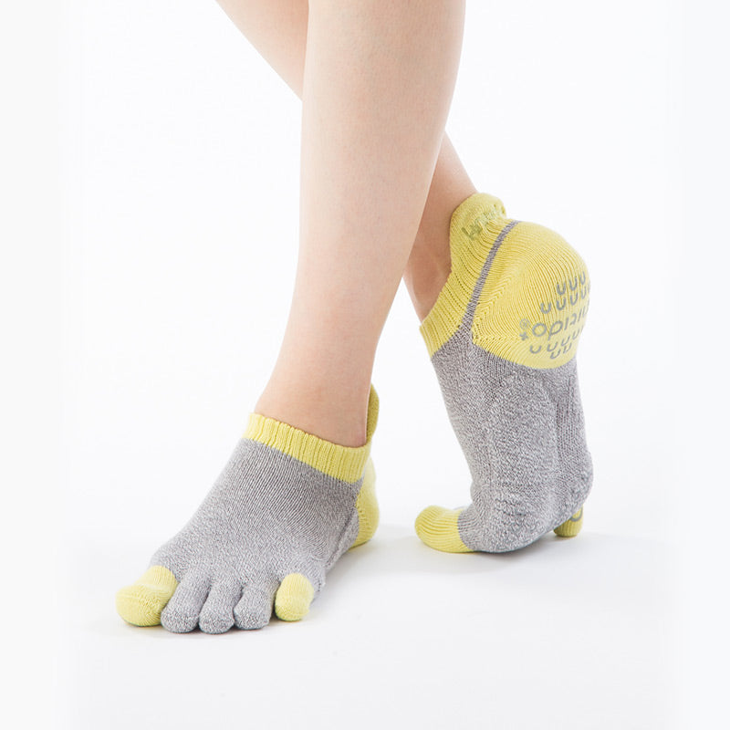 An oblique view of a leg wearing a pair of Knitido plus brand Two Colors Footie Grip Toe Socks With Power Pads in Grey and Yellow